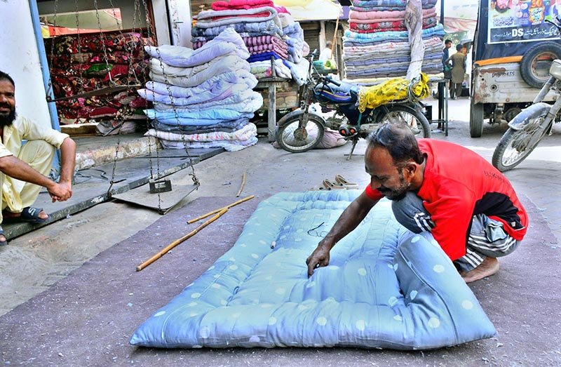A worker hand-stitches a quilt for customers at his workplace as demand rises ahead of the winter season.
