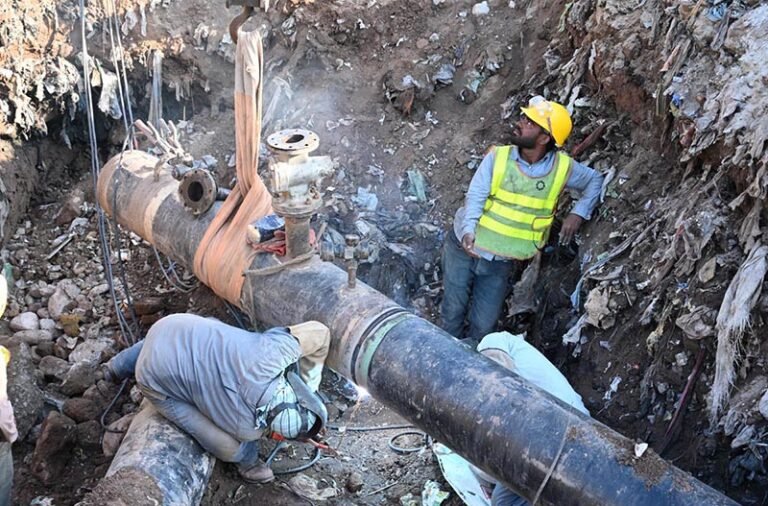 Workers weld a large gas pipeline in a deep trench as a crane holds the pipe in position during repair work in the Federal Capital