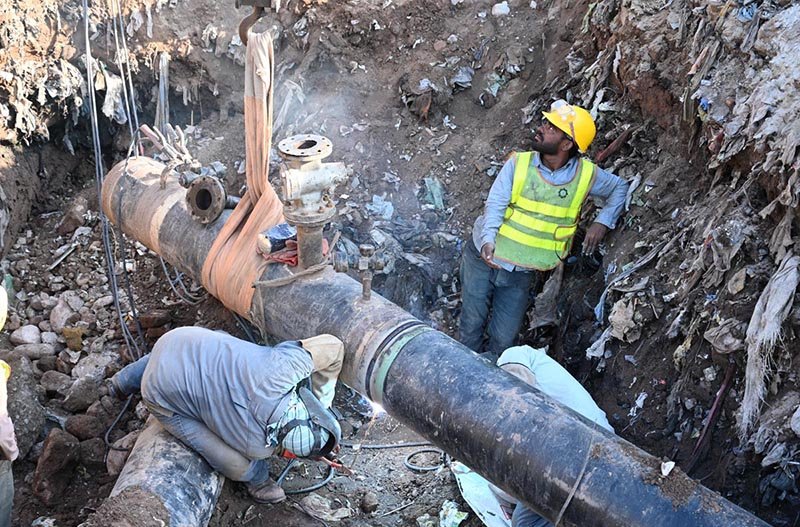 Workers weld a large gas pipeline in a deep trench as a crane holds the pipe in position during repair work in the Federal Capital