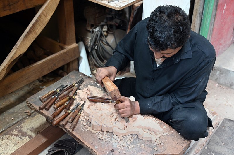 A craftsman carves a decorative design into a piece of wood at his workshop in the Pindora area