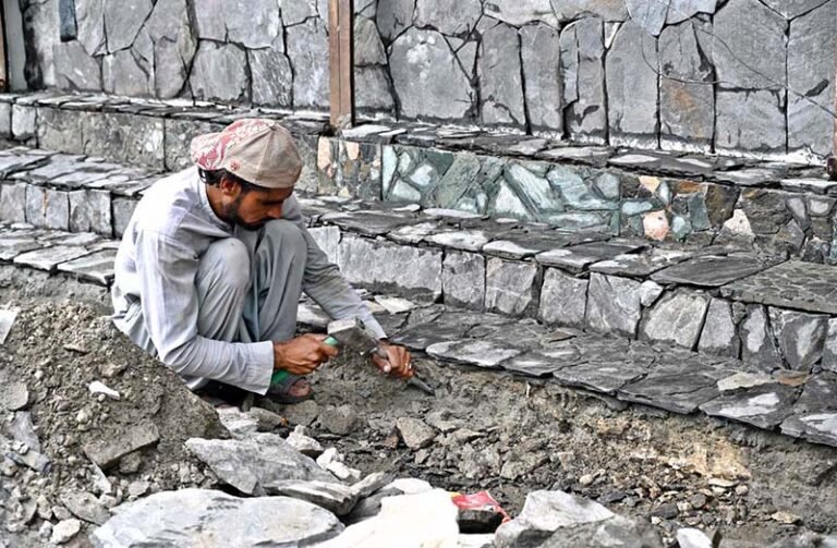 A labourer is working with a chisel and hammer to dress stones.