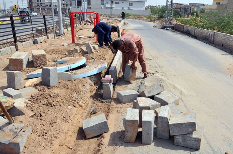 Labourers install concrete blocks along the roadside as part of ongoing road and drainage development work