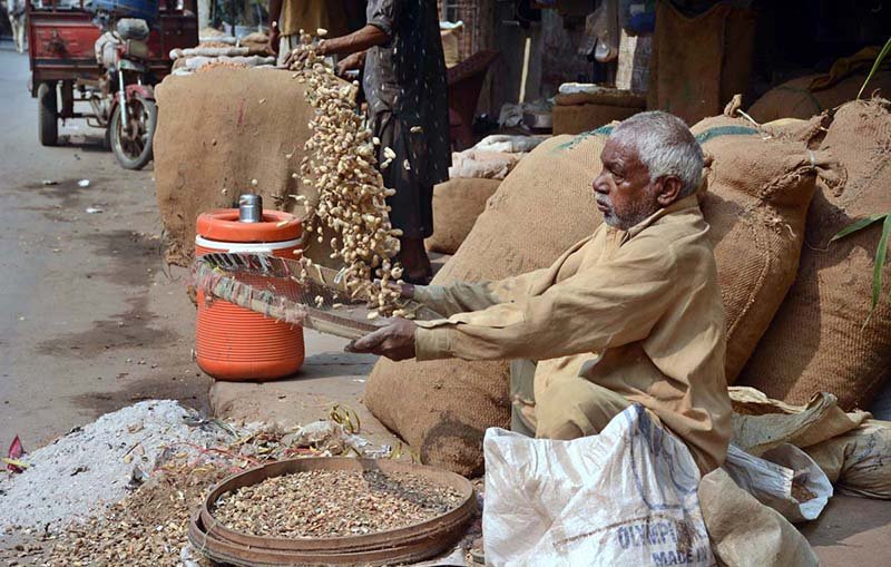 A worker cleans peanuts using a traditional method at a grain market to attract customers.