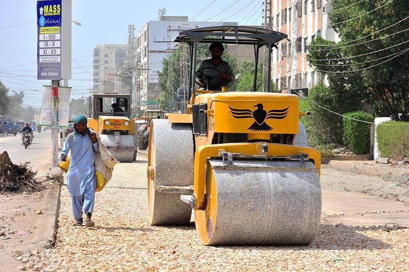 A heavy machinery operator uses a road roller to level a newly constructed road during ongoing development work at Latifabad Unit No. 09.