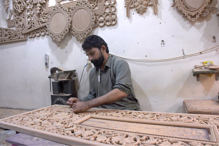 A skilled man carving wood of a furniture piece at his workplace