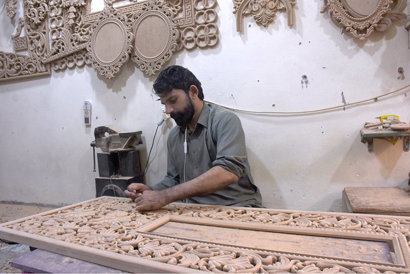 A skilled man carving wood of a furniture piece at his workplace