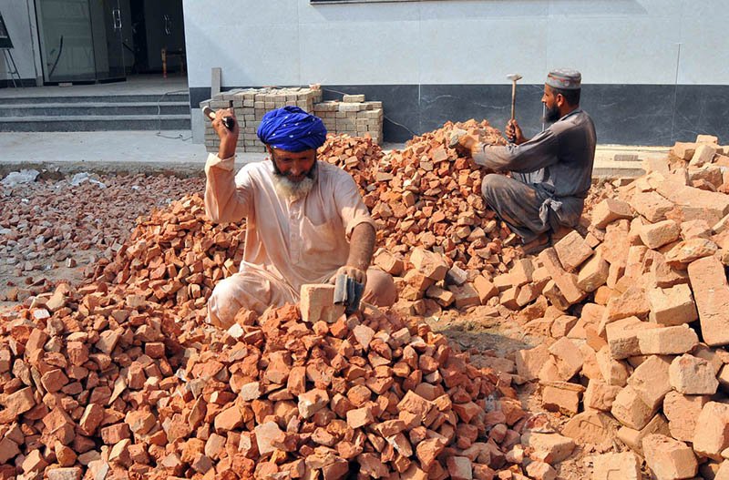 Labourers break bricks into smaller pieces using hammers at a construction site, earning their livelihood through manual labour.