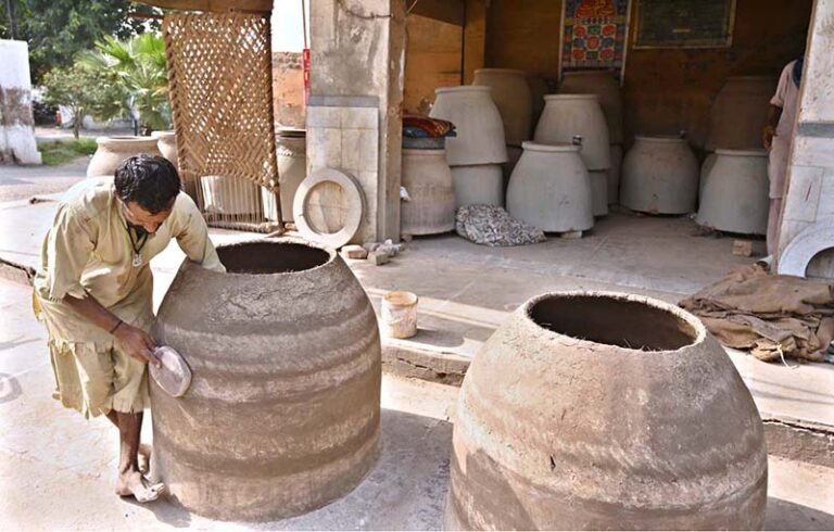 A potter gives the final shape and finishing touches to a traditional tandoor at his workplace near Railway Chowk