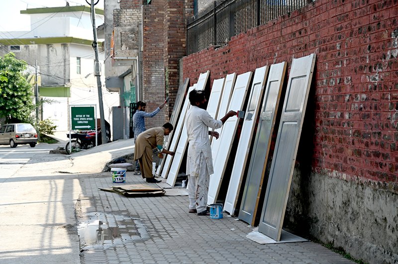 Carpenters and painters painting wooden doors meant for construction use, beside the road