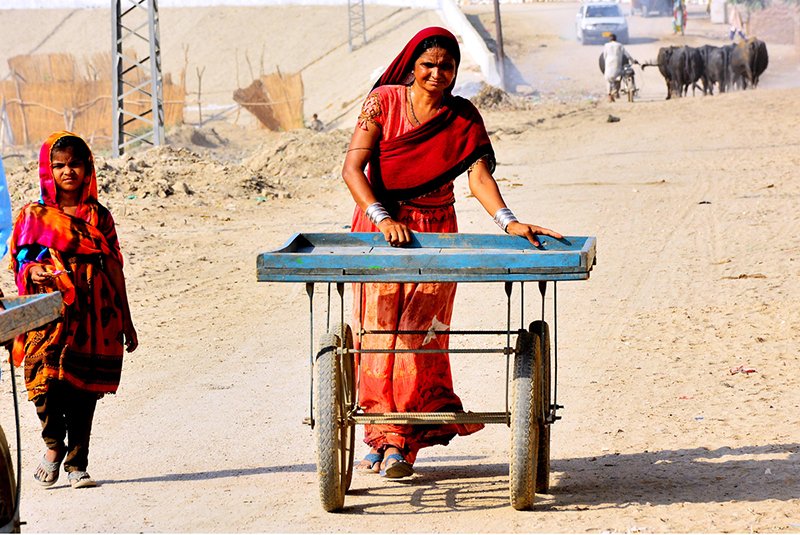 A woman from a nomadic community pushes an empty handcart with her daughter along a street in Latifabad Unit No. 4.