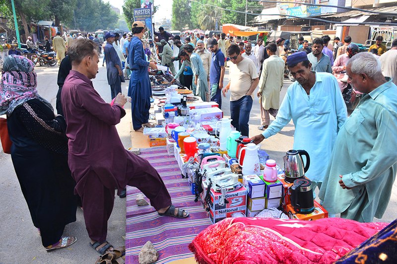 Customers browse and purchase electronic items from vendors at a Friday bazaar.