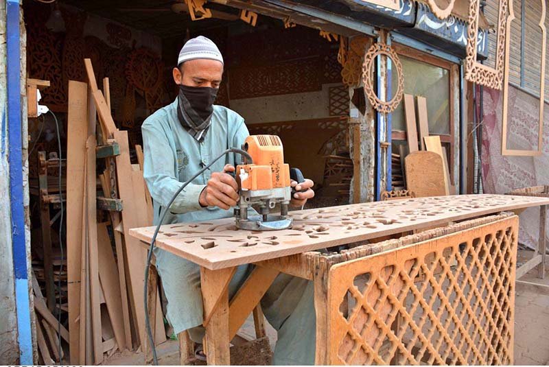 A carpenter busy in carving different designs on hardboard sheet at his workplace
