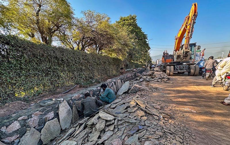 Labourers construct a boundary wall along the road at the Kashmir Chowk Underpass Project site in the federal capital.