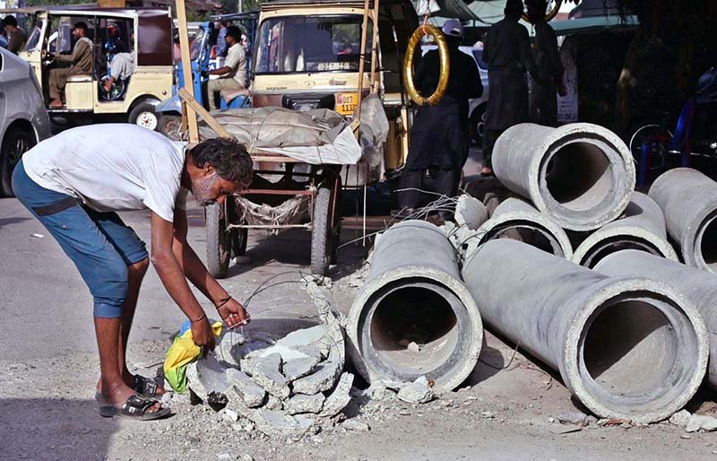 A drug addict removes iron from a discarded sewerage pipe lying on Mission Road in the old city area, highlighting the need for greater attention by the concerned authorities