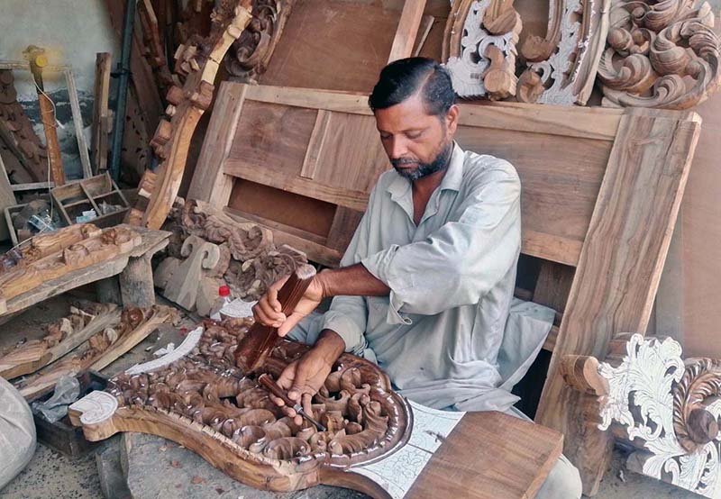 A furniture worker carves intricate designs on wood at his workplace