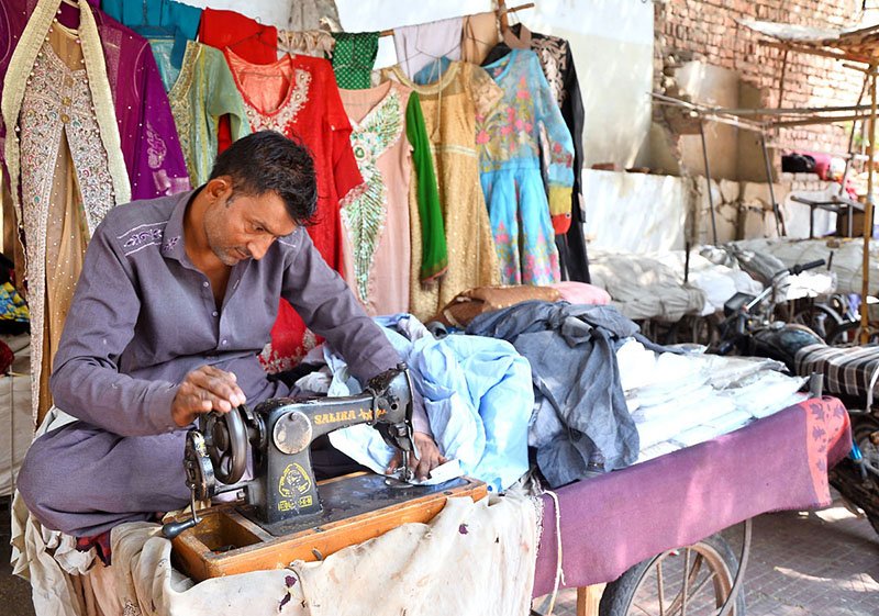 A roadside tailor stitches women’s dresses on his setup at a cloth market in the city.