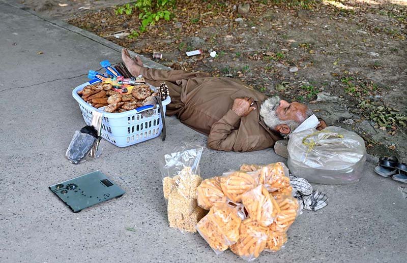 An elderly vendor taking a nap on the footpath in the shade of a tree in the Federal Capital