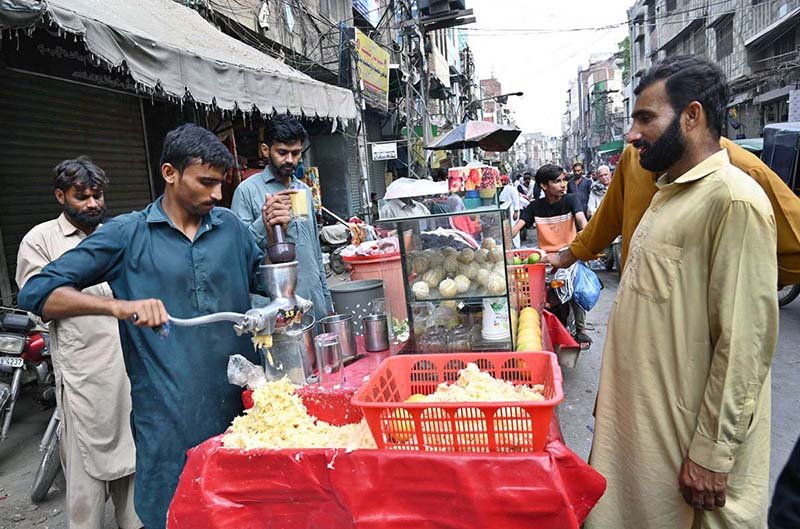 People drink fresh juice made from seasonal mausambi (sweet lime) prepared by a fruit vendor