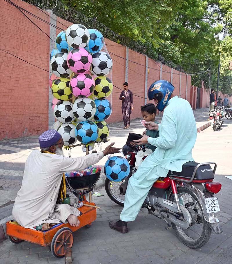 An elderly, disabled vendor sells balls by the roadside to earn a livelihood for his children in the city