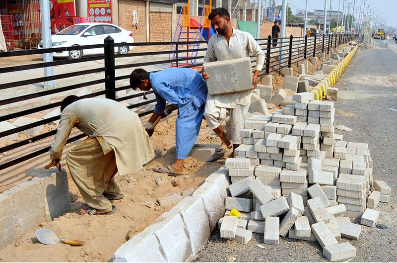 Labourers install concrete blocks along a roadside footpath as part of ongoing development work in the city.