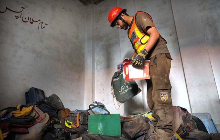A Rescue 1122 official collects the belongings of schoolchildren from the rubble of a collapsed school building in Dir Colony, where several students were killed and injured.