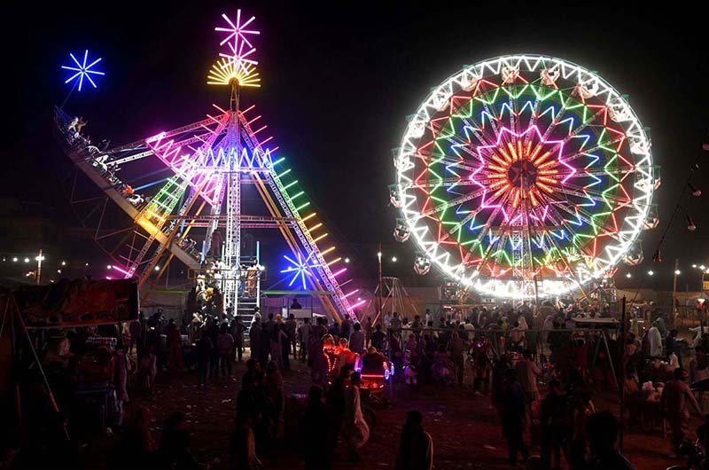 People watch and enjoying a Ferris wheel at night with colorful light during a Dada Hanjer Pir local mela festival at fair ground near Multan road