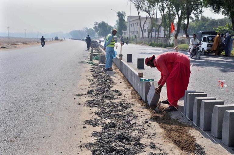 Workers installing concrete blocks as a divider during construction of a road from Shahbaz Building to Latifabad Road as part of development work