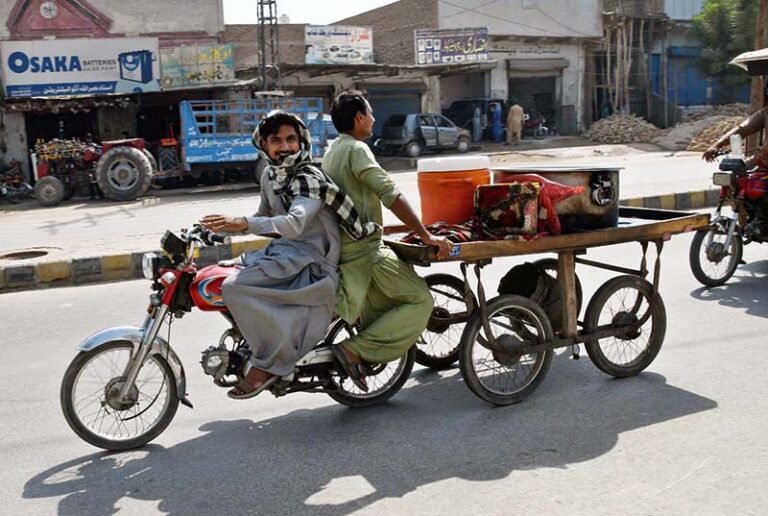 Motorcyclists tow a handcart along Sheikh Zayed Colony Road.