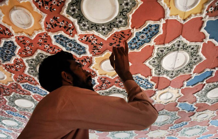 A skilled artisan meticulously paints intricate floral and geometric patterns on a ceiling, showcasing the rich tradition of decorative ceiling art that has been an integral part of Pakistan’s architectural heritage for centuries