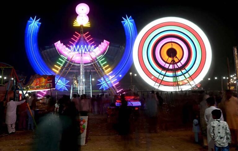 People watch and enjoying a Ferris wheel at night with colorful light during a Dada Hanjer Pir local mela festival at fair ground near Multan road