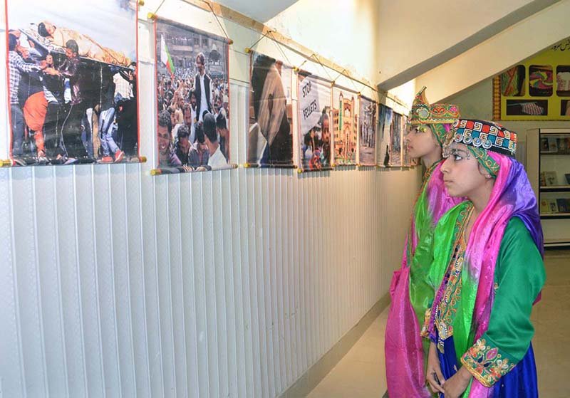 Children dressed in Kashmiri attire view photographs depicting alleged Indian atrocities against the Kashmiri people during a Kashmir Black Day event at the Arts Council.