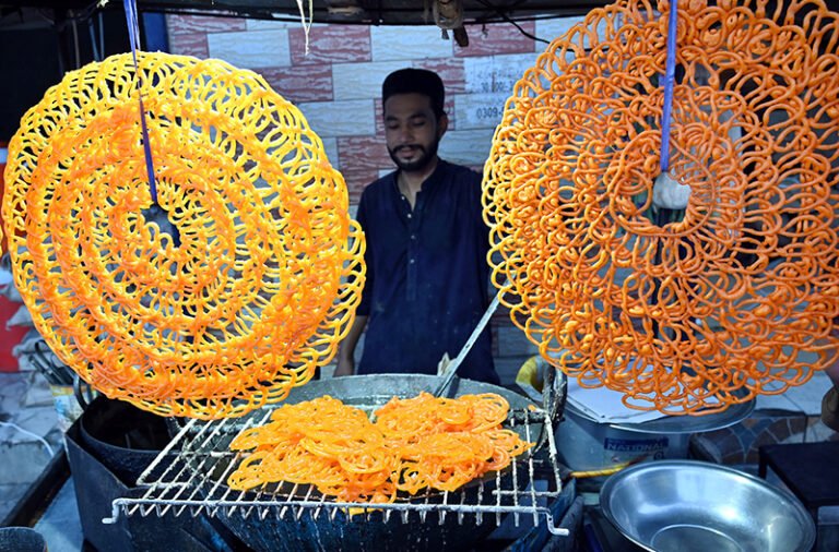 A vendor preparing the traditional sweet food item (Jalebi) to the customer on the roadside setup in the Provincial Capital.