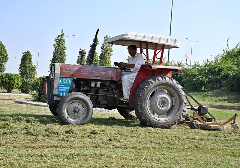 A CDA worker uses a tractor-mounted mower to trim grass along the green belt at Faizabad Interchange