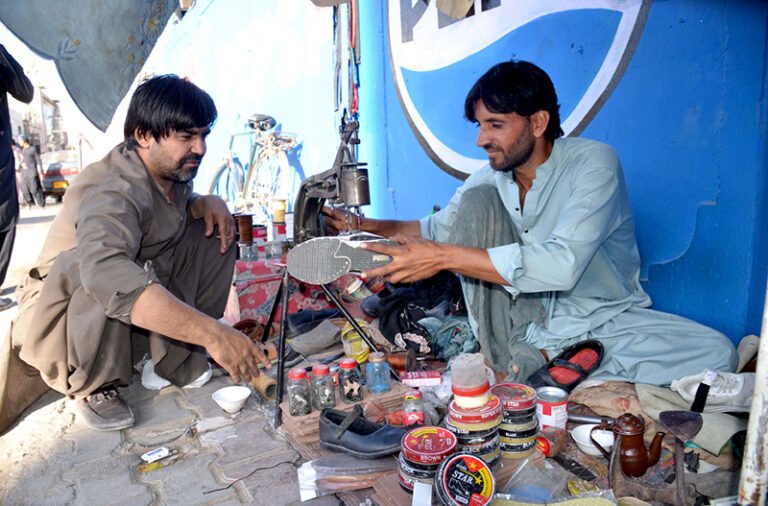 – Cobbler preparing damaged shoos of its customer who sitting near him at Jinnah Road.