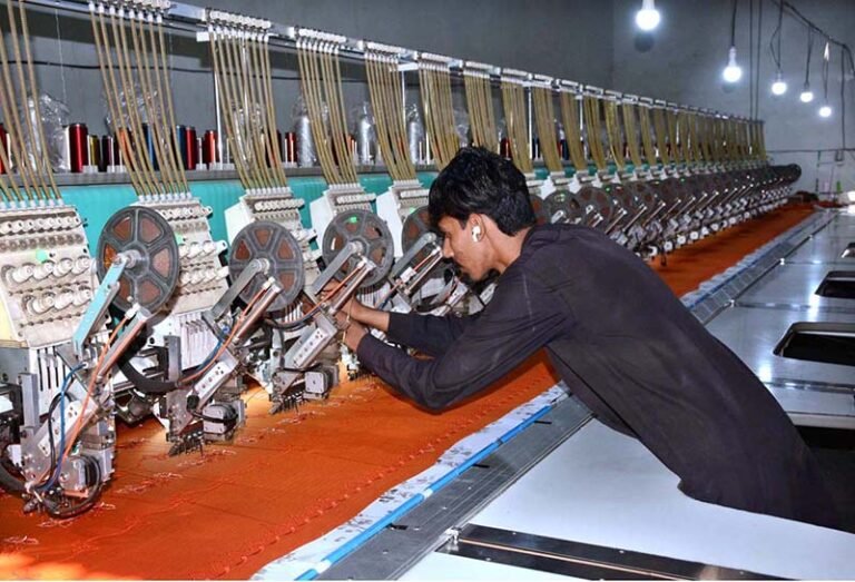 A worker monitors fabric embroidery on a computerized machine at a local factory