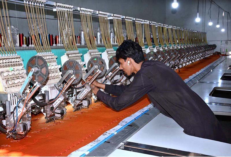 A worker monitors fabric embroidery on a computerized machine at a local factory