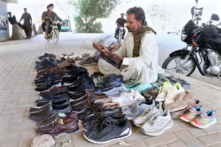 A vendor polishes used shoes displayed on the sidewalk to attract customers looking for low-priced footwear.