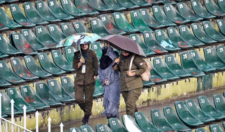 Women police officials shield themselves with umbrellas from the rain before the start of the third T20 cricket match between Pakistan and Sri Lanka at Rawalpindi Cricket Stadium