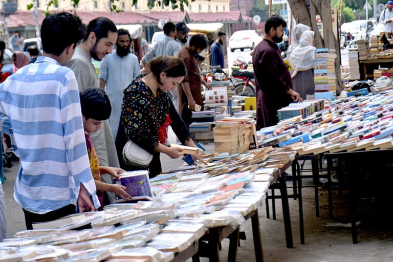 People selecting and purchasing old books from a roadside setup at Mall Road