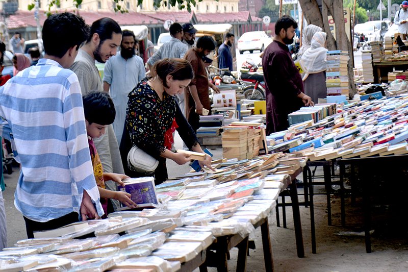 People selecting and purchasing old books from a roadside setup at Mall Road