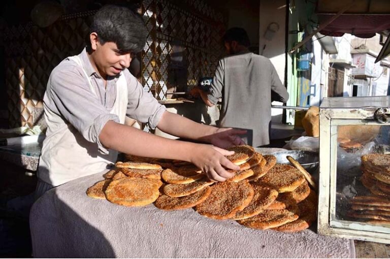 A worker displays freshly baked roghni naan for sell at a tandoor