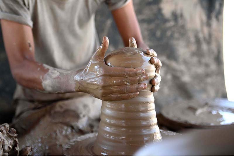 A potter shapes red clay with his fingers while spinning it on a wheel to make a vase for floral arrangements at a workshop in New Karachi